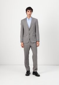 Completo grigio su misura con giacca a un bottone, pantaloni dritti e camicia azzurra chiara. Scarpe nere completano l'outfit.