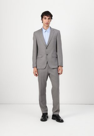 Gray tailored suit with a single-button blazer, straight-cut trousers, and light blue shirt. Black shoes complete the ensemble.