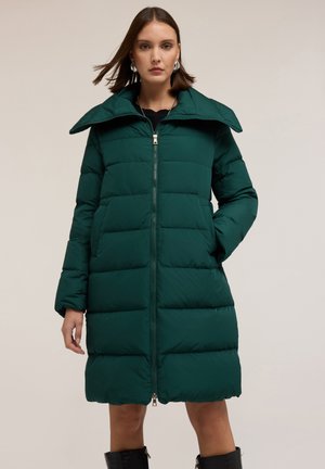 Groene pufferjas met een hoge kraag, ritssluiting, gewatteerde textuur en lange mouwen. Ontworpen met zakken en een lengte tot onder de knie.