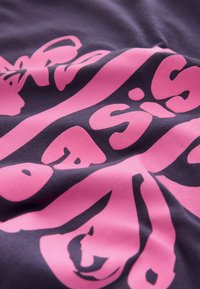 Dark fabric with prominent pink text in a bold, rounded font. The design features varying thicknesses and curves, creating dynamic visual interest.