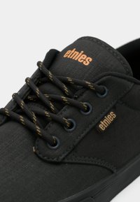 Μαύρες καμβά παπούτσια αθλητικά με υφασμάτινη επιφάνεια, διαθέτουν μαύρες κορδόνες με κίτρινες λεπτομέρειες, μεταλλικά μάτια και πορτοκαλί λογότυπο στο πλάι.