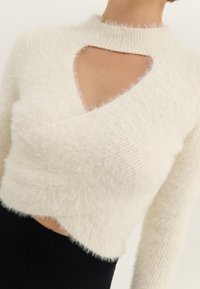 Maglione bianco in maglia morbida e pelosa con un profondo scollo sul petto. Presenta un collo alto e maniche lunghe, la texture è soffice e vellutata.