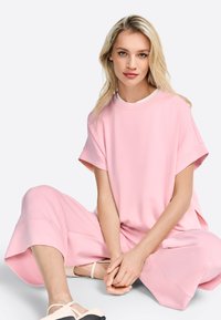 Světle růžový oversized top s krátkými rukávy a kulatým výstřihem, v kombinaci s odpovídajícími širokými kalhotami. Měkký materiál, volný střih.