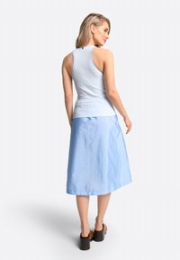 Hellblauer Rock mit glatter Textur, kombiniert mit einem ärmellosen gestreiften Oberteil in Blau und Weiß. Dicke braune Plateauschuhe.