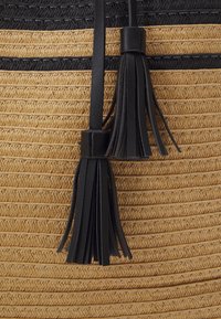 Sac en paille rond avec des motifs tissés alternés de couleur tan et noir, accentué de franges en cuir noir et de anses.