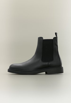 Schwarzer Lederknöchelstiefel mit elastischer Seitenpartie und Zuglasche, flacher Sohle und abgerundetem Zehenbereich, seitlich auf neutralem Hintergrund gezeigt.