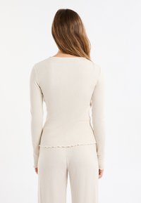 Top a maniche lunghe a coste color beige chiaro con scollo rotondo e orlo ondulato, abbinato a pantaloni a coste coordinati, texture morbida.