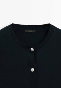 Cardigan en maille noire avec encolure ronde et deux boutons argentés embossés sur la patte de boutonnage avant, étiquette à l'intérieur du col.