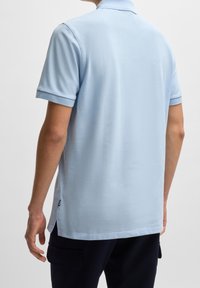 Polo bleu clair en tissu doux, avec un col pointu et des manches courtes. Le bas comporte des fentes sur les côtés pour le confort.