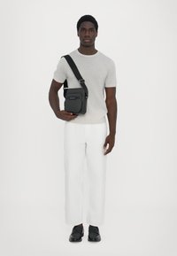Borsa a tracolla nera con motivo testurizzato, t-shirt grigia in maglia, pantaloni bianchi a gamba larga e scarpe nere slip-on. Design semplice e moderno.