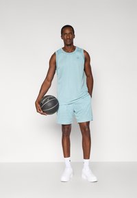 Vaaleansininen verkkokangasinen toppi ja shortsit, joissa on rento istuvuus. Malli pitää kädessään mustaa koripalloa valkoisilla yksityiskohdilla ja hänellä on jalassa valkoiset lenkkarit.