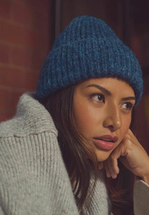 Sinine kudum beanie ribitud tekstuuriga. Tumedashall, üle mõõtme sweatshirt osaliselt nähtav. Taust udune, keskendudes peadele ja õlgadele.