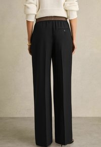 Pantaloni neri a gamba larga con una texture liscia. Vita elasticizzata, dettagli marroni e una singola tasca posteriore con bottone.