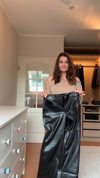 Black faux leather pants with a smooth, shiny surface, featuring a button and zipper closure, front pockets, and a relaxed fit.