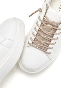 White leather sneakers with a smooth texture, featuring metallic gold laces and a minimalist design. Rounded toe and contrasting sole.