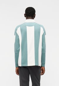 Πουκάμισο με μακριά μανίκια και εναλλασσόμενες κάθετες ρίγες σε ανοιχτό μπλε και λευκό, με διακοσμητικά στους ώμους και επιθέματα στους αγκώνες, κατασκευασμένο από απαλό βαμβάκι.