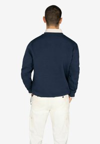 Sudadera azul marino con cuello redondo, puños de canalé y un acabado texturizado, combinada con pantalones cargo crema con bolsillos laterales.