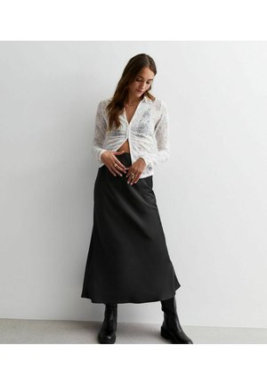 Blusa blanca de encaje de manga larga con botón delante, combinada con una falda negra de satén en corte A y botas negras de tobillo. Diseño simple y elegante.