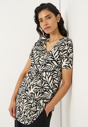Schwarz- und crema-farben gemusterte kurzärmelige Bluse mit V-Ausschnitt und gerafft Detail an der Taille, die ein florales Design zeigt.