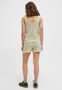 Randig jumpsuit i kräm- och brunstickad tyg, med en rundad rygg och luftig passform, som slutar vid mitten av låret. Bärs med mörka skor och grå strumpor.