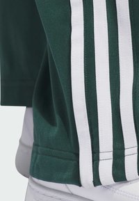 Zelena atletska majica z belimi vertikalnimi črtami ob straneh. Tkanina ima teksturiran zaključek in prilegajoč design na robu.