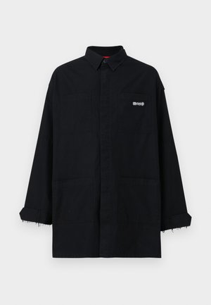 Sort oversized skjorte med krave, udstyret med to frontlommer og flossede manchetter. Fremstillet af robust stof med subtil branding på brystet.