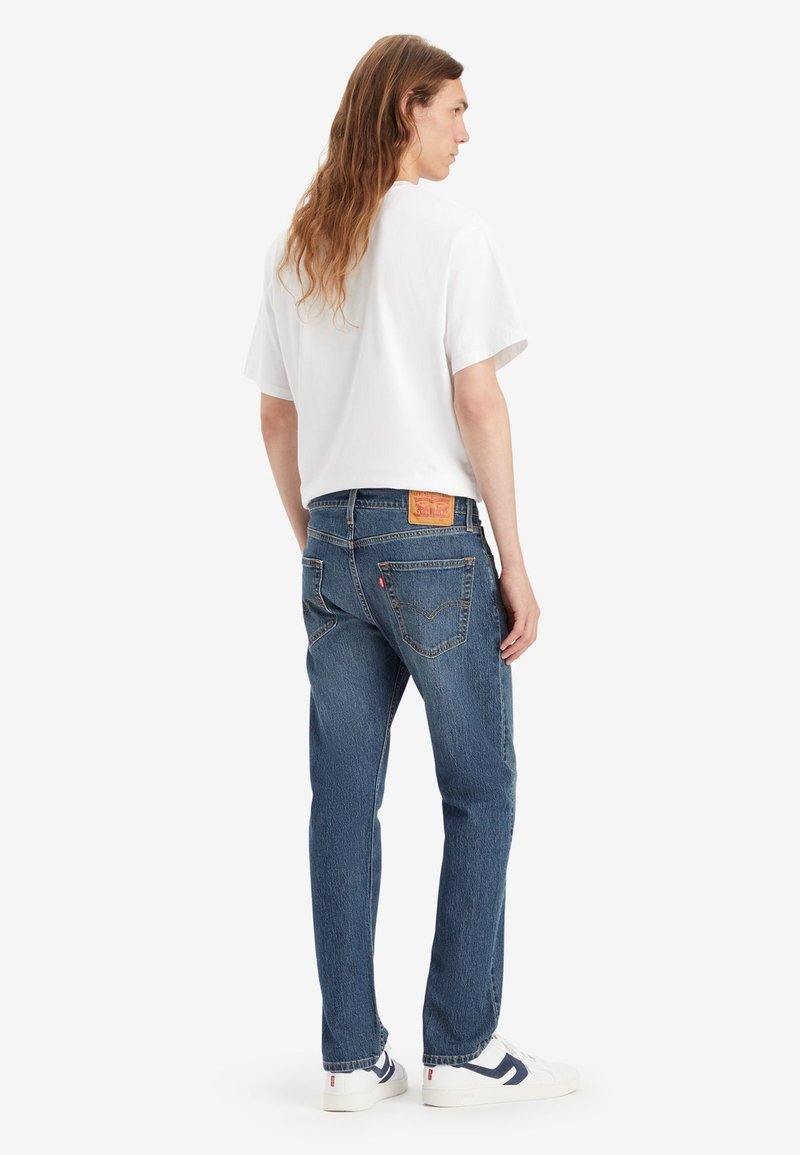 Weißes T-Shirt mit kurzen Ärmeln, kombiniert mit dunkelblauen Jeans mit Leder-Patch, geradem Bein und klassischem Taschen design.
