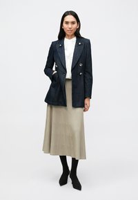 Μπλε σκούρο τζιν σακάκι με διπλή σειρά κουμπιών, σε συνδυασμό με λευκό μπλουζάκι και μπεζ πλισέ φούστα. Μαύρες καλτσοδέτες και μυτερές παπούτσια ολοκληρώνουν την εμφάνιση.