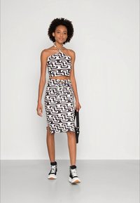 Conjunto de duas peças em padrão preto e branco, apresentando um top cropped de halter e uma saia até ao joelho, acompanhado de ténis pretos. Textura de tecido suave.