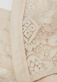 Light beige lingerie fabric featuring intricate lace patterns, elastic bands, and multiple hook-and-eye closures along the edge.