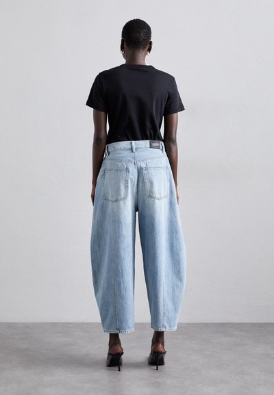 Ανοιχτό μπλε φαρδύ τζιν παντελόνι με ψηλή μέση, πίσω τσέπες και καθαρό φινίρισμα. Συνδυάζεται με εφαρμοστό μαύρο μπλουζάκι και ψηλοτάκουνες γόβες.