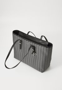 Black and white patterned tote bag with a structured shape, smooth leather accents, dual handles, and a metal logo charm. Zippered closure.