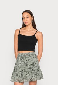 Top cropped preto com alças finas, combinado com uma saia verde clara em camadas com um padrão de manchas pretas.
