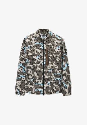 Takki, joka on kamouflagekuvioinen ja jossa on beige, musta ja sininen muotoilu, täysipituinen vetoketju edessä ja rintatasku vetoketjulla, jossa on ruskea reunus.