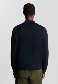 Mörkblå stickad tröja med långa ärmar och krage. Har en slät yta och en avslappnad passform, passar bra till olivgröna byxor.