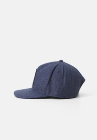 Casquette snapback bleu foncé en tissu texturé, avec une visière plate et un petit patch logo sur le côté gauche à l'avant.