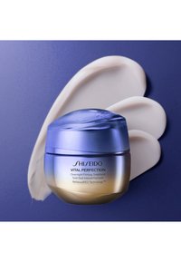 Shiseido Vital Perfection nattkrem i en rund krukke med blå gradientlokk og gullfarget bunn, ledsaget av en kremete hvit produktprøve.