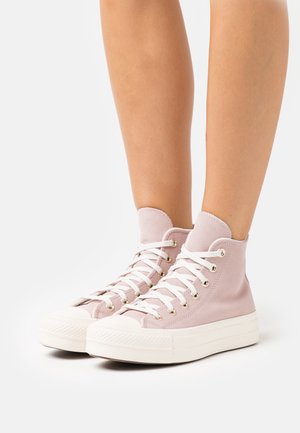 Jasnoróżowe trampki typu high-top, wykonane z zamszu, z białymi sznurówkami i złotymi oczkami; teksturowana gumowa podeszwa; minimalistyczny design.