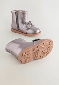 Metallic pink støvler med lynlås i siden, sløjfe detalje og gummisål med textur i et sløjfe mønster. Blødt kunstpelsfor indeni.