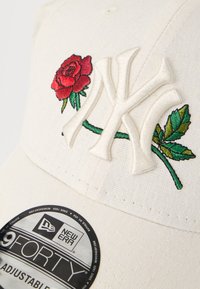 Λευκό καπέλο με κεντημένο λογότυπο της Νέας Υόρκης σε κρεμ χρώμα, κόκκινα τριαντάφυλλα και πράσινα φύλλα. Διαθέτει υφασμάτινη υφή και ρυθμιζόμενο λουράκι.