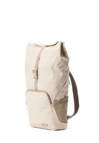 Beige Stoffrucksack mit Rollverschluss, verstellbarem Tragegurt und einer vorderen Reißverschlusstasche. Texturierte Akzente verleihen dem Design visuelles Interesse.