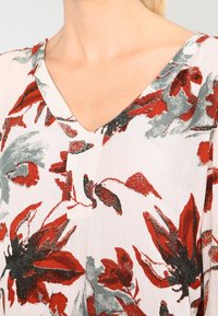Flowy, lightweight top with a V-neck, featuring red and gray floral patterns on a white background. Soft, textured fabric.