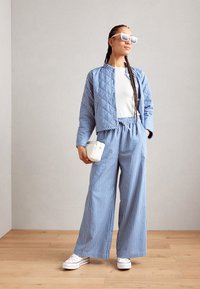 Prešívaná svetlomodrá pruhovaná bunda s okrúhlym krkom, doplnená širokými pruhovanými nohavicami. Pár bielych tenisiek a malá biela taška dotvárajú outfit.