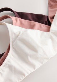 Trois masques faciaux en tissu doux blanc, rose poudré et brun foncé, superposés sur une surface claire.