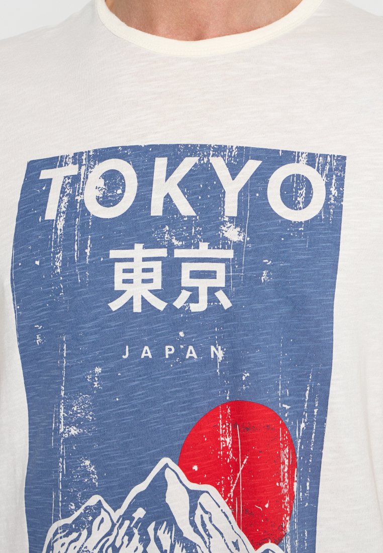 Biała koszulka z niebieską grafiką z napisem "TOKYO" oraz japońskimi znakami, czerwoną słońce i stylizowanymi górami w zniszczonym wzorze.