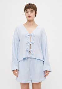 Lyseblå, struktureret bomuldsbluse med V-udskæring, udstyret med en frontknude og lange, brede ærmer, kombineret med matchende shorts.