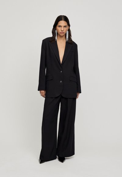 Black tailored blazer with a deep V-neck and two buttons, paired with wide-leg black trousers. Smooth fabric with minimal detailing.
