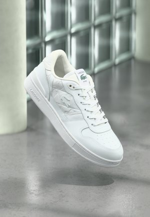 Weißer Ledersneaker mit strukturiertem Design und perforierter Zehenpartie, ausgestattet mit einer Gummisohle, Schnürverschluss vorne und grünem Logo an der Ferse.