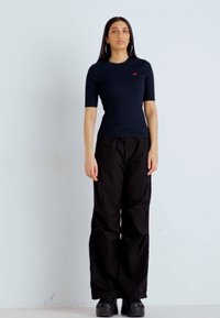 Pantalons cargo noirs à coupe ample, associés à un haut ajusté à manches courtes bleu marine avec un logo rouge. Design simple, sans motifs notables.