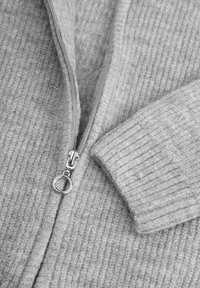 Jasnoszary sweter z dzianiny z zamkiem błyskawicznym i ściągaczami na rękawach. Tkanina ma miękką teksturę z delikatnym wzorem.